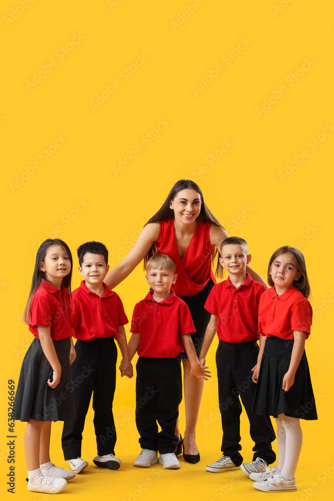 Little school children with female teacher on yellow background