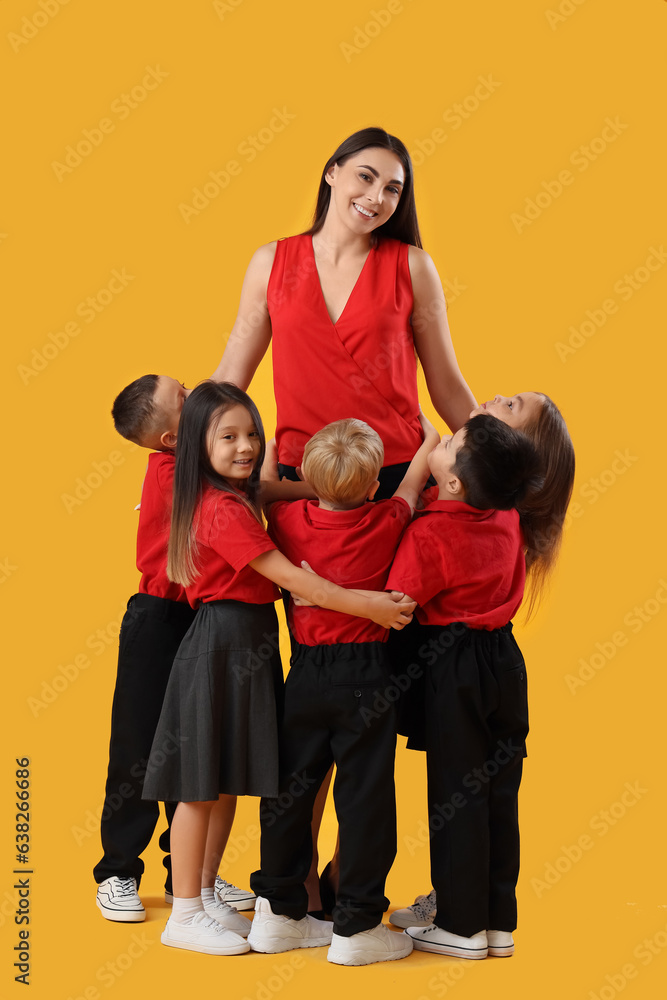 Little school children with female teacher on yellow background