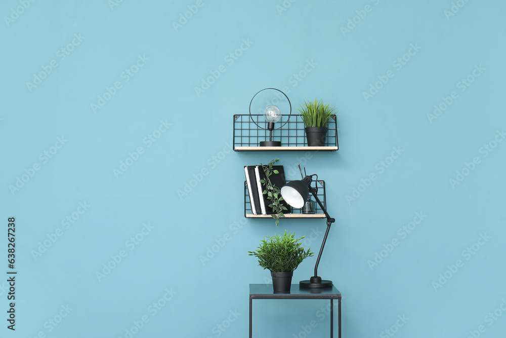 Desk lamp and houseplant on small table near blue wall