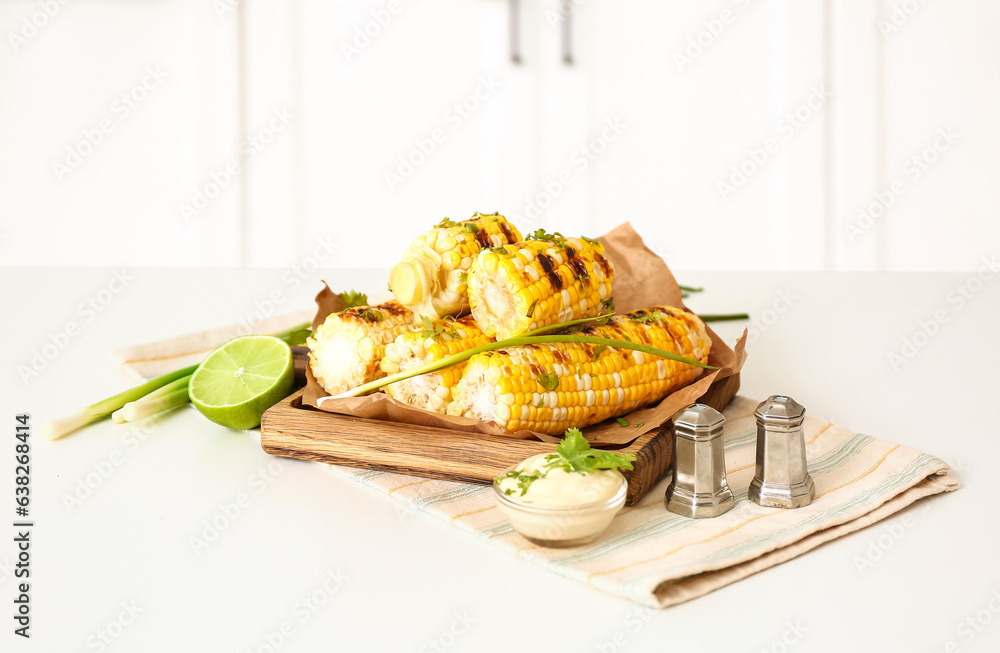 Wooden board with tasty grilled corn on table in kitchen