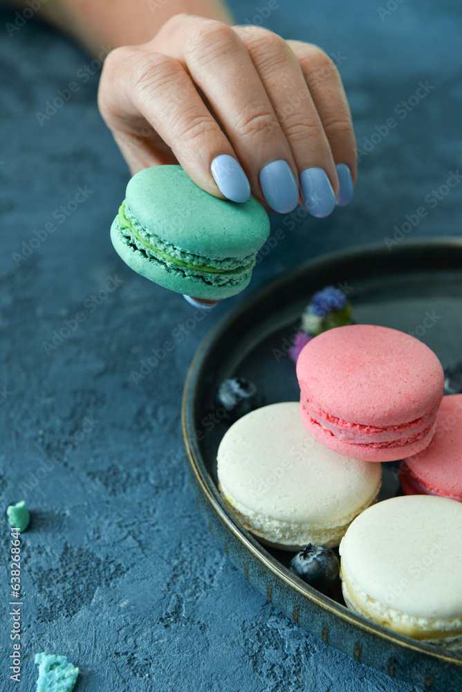 Woman holding sweet macaroon on blue background