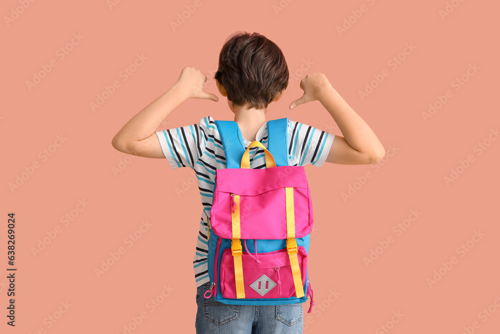 Little boy pointing at backpack on color background