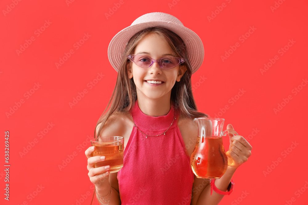 Little girl with glass and jug of juice on red background