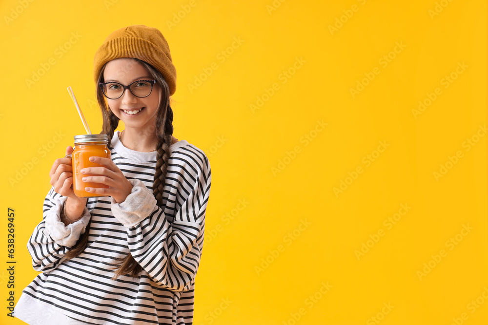 Little girl with glass jar of juice on yellow background