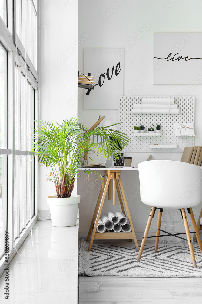 Interior of light office with workplace, pegboard and houseplants