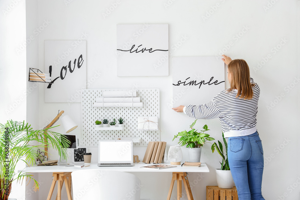 Young woman with poster on light wall in office, back view