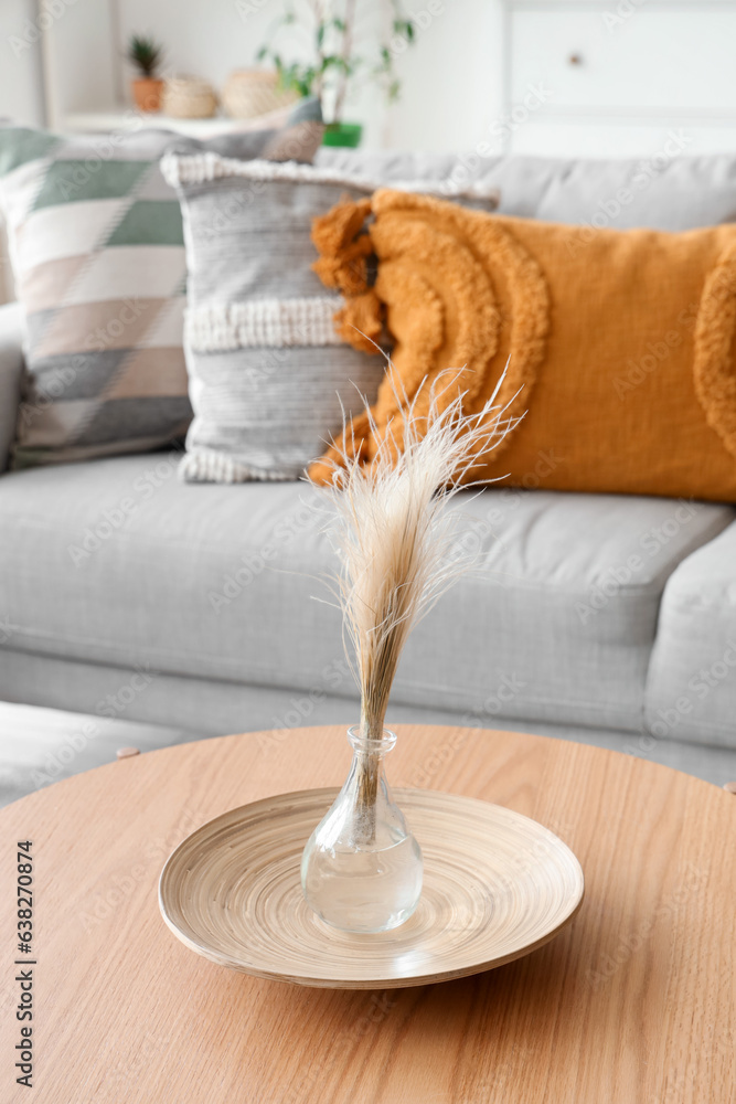 Vase with dried grass on wooden coffee table in living room, closeup