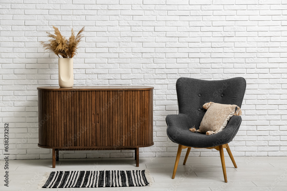 Stylish armchair and wooden cabinet near light brick wall