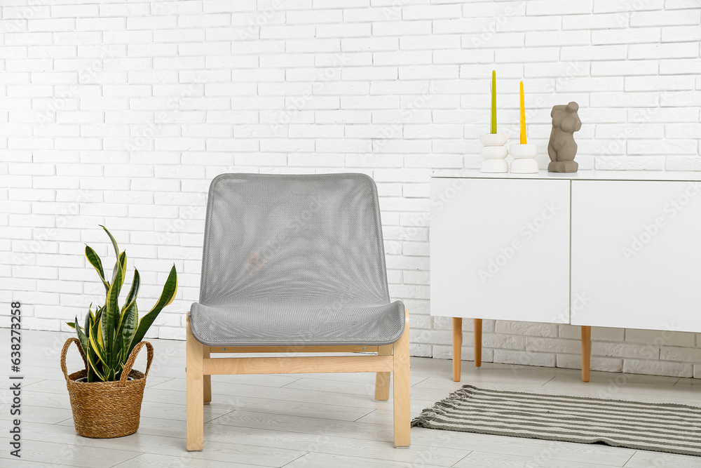 Stylish armchair, houseplant and cabinet with decor near light brick wall