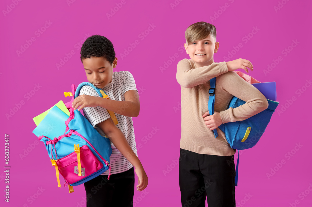 Little classmates in stylish uniform with notebooks and backpacks on purple background