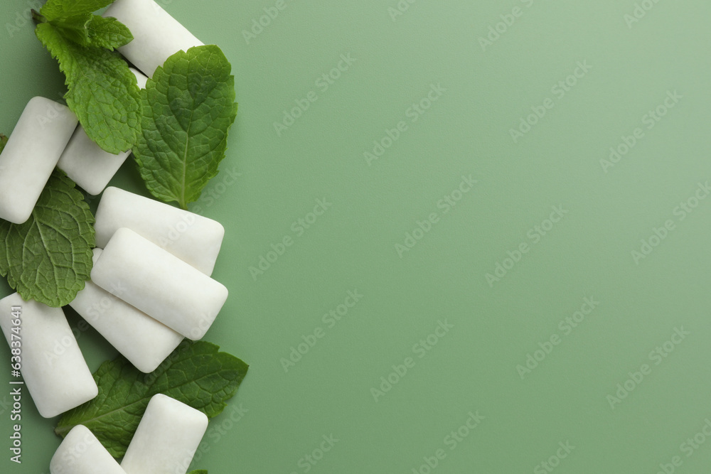 Tasty white chewing gums and mint leaves on light green background, flat lay. Space for text