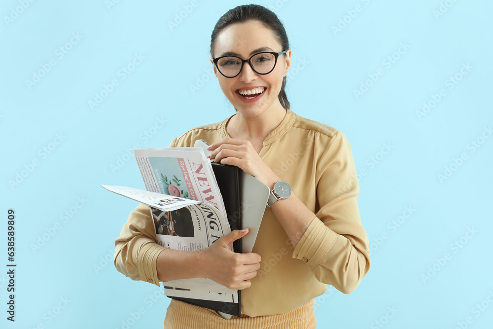 Young businesswoman with wristwatch, newspapers and laptop on blue background