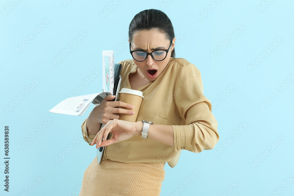 Shocked young businesswoman with wristwatch and cup of coffee on blue background