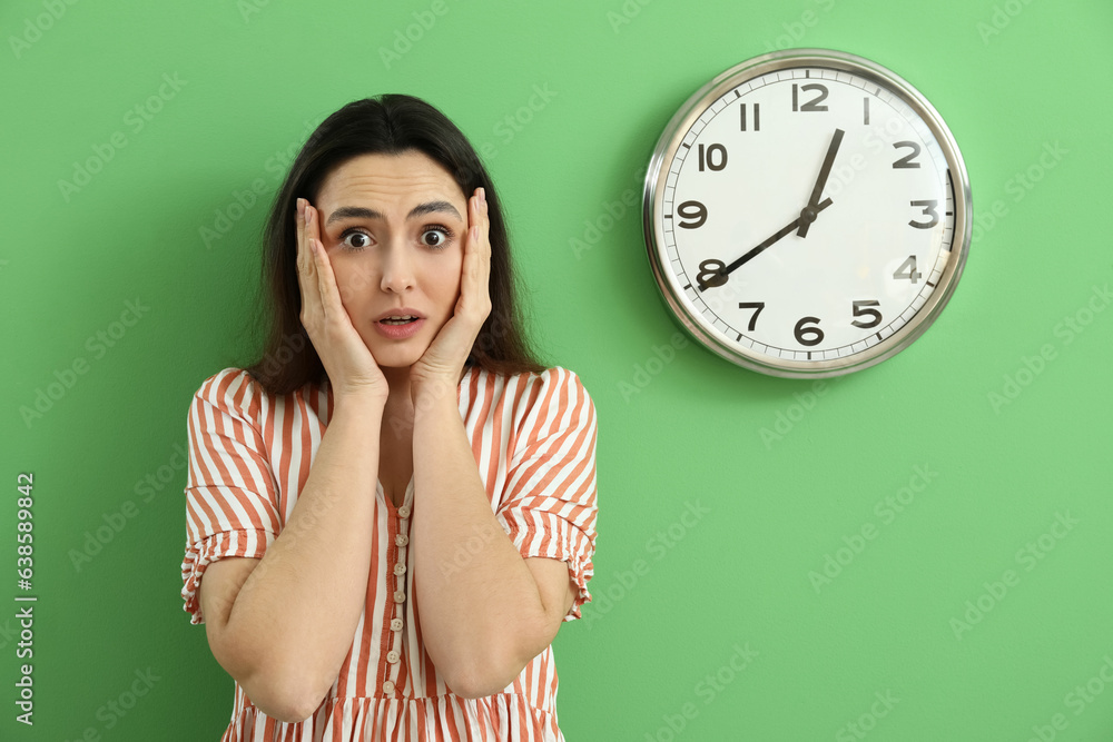 Shocked young woman and clock on green wall