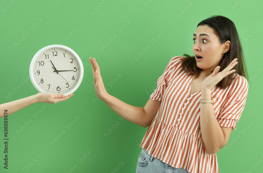 Shocked young woman with wall clock on green background