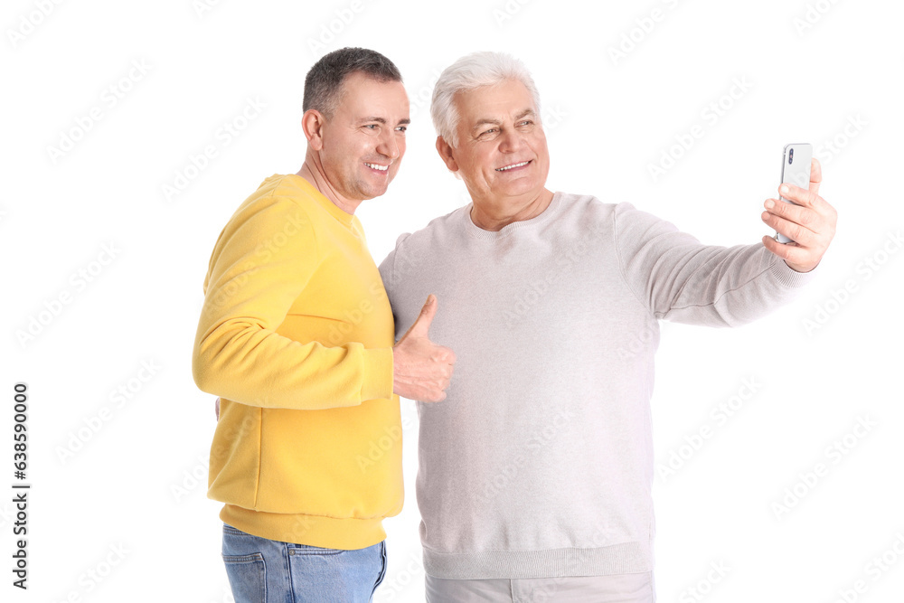 Mature brothers with mobile phone taking selfie on white background