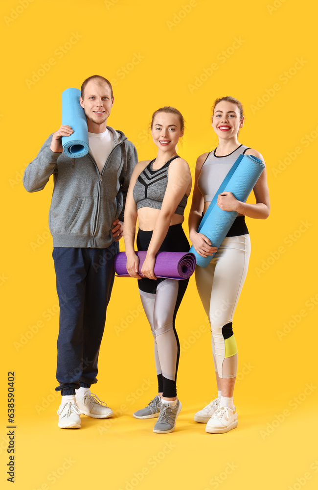 Sporty young people with fitness mats on yellow background