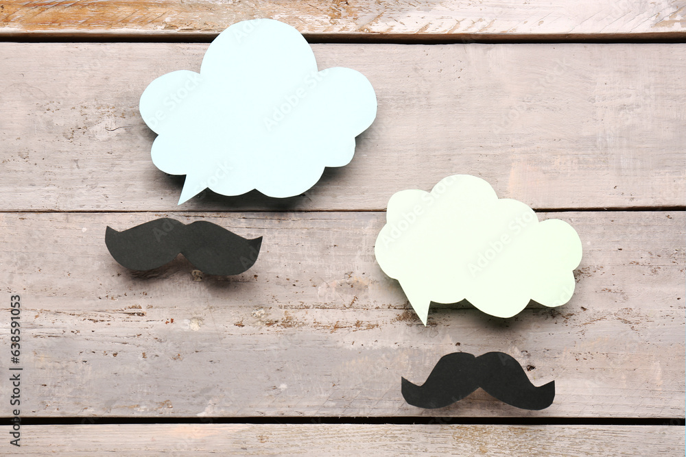 Paper mustaches with blank speech bubbles on grey wooden background