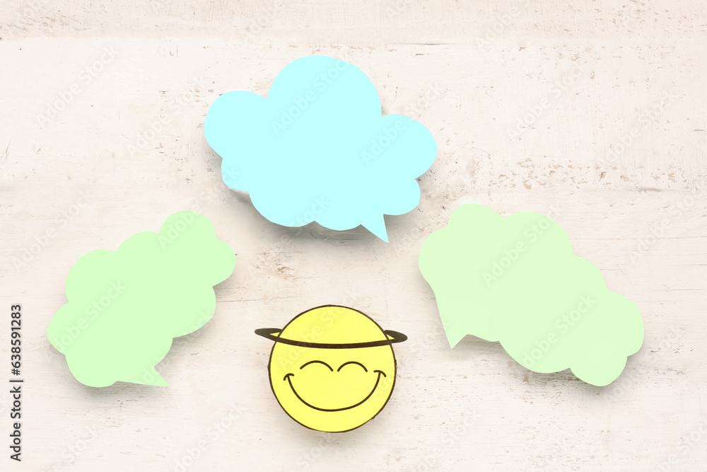 Paper face with blank speech bubbles on beige wooden background