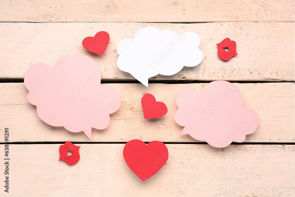 Paper lips and hearts with blank speech bubbles on beige wooden background