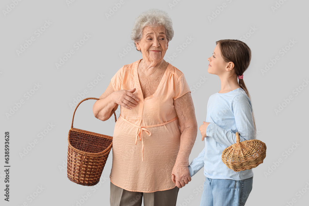 Little girl with her grandmother and baskets on grey background