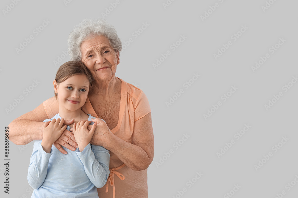 Little girl with her grandmother hugging on grey background