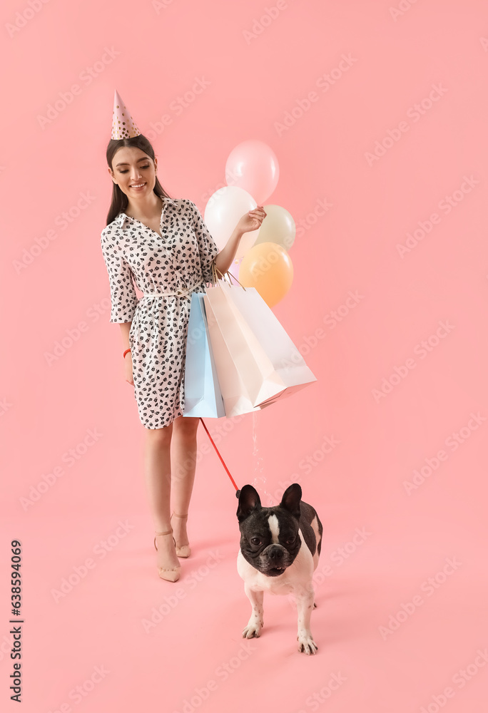 Young woman with her French bulldog, shopping bags and balloons on pink background