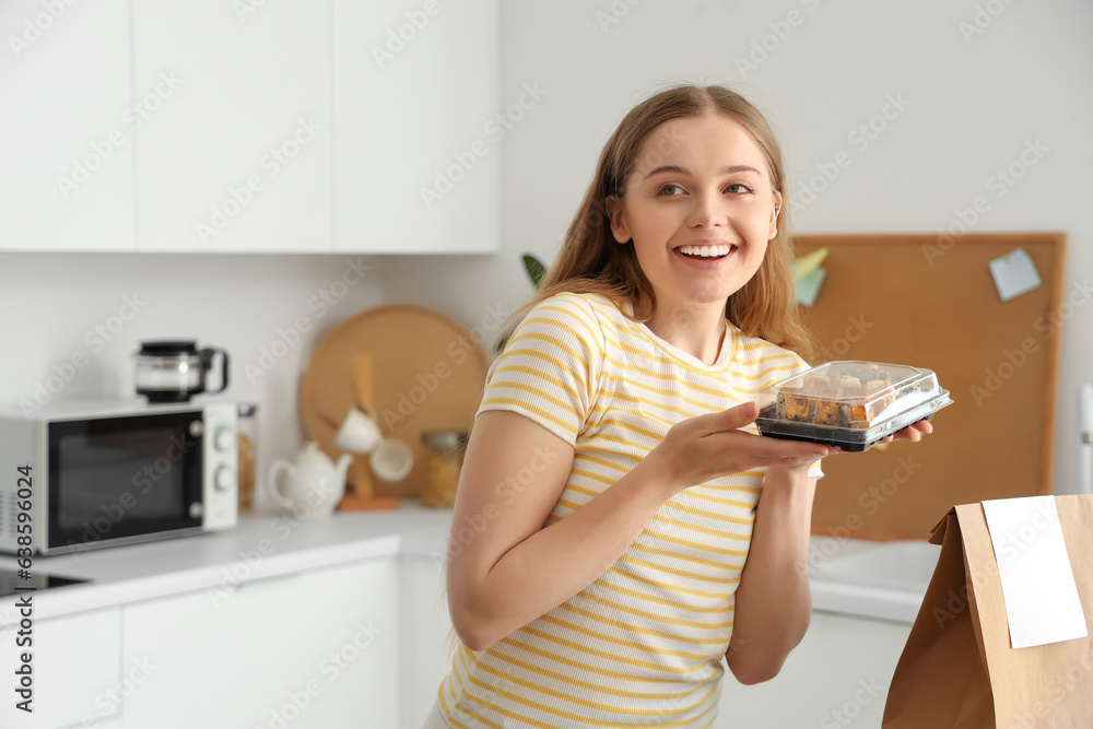 Happy young woman with sushi and paper bag in kitchen