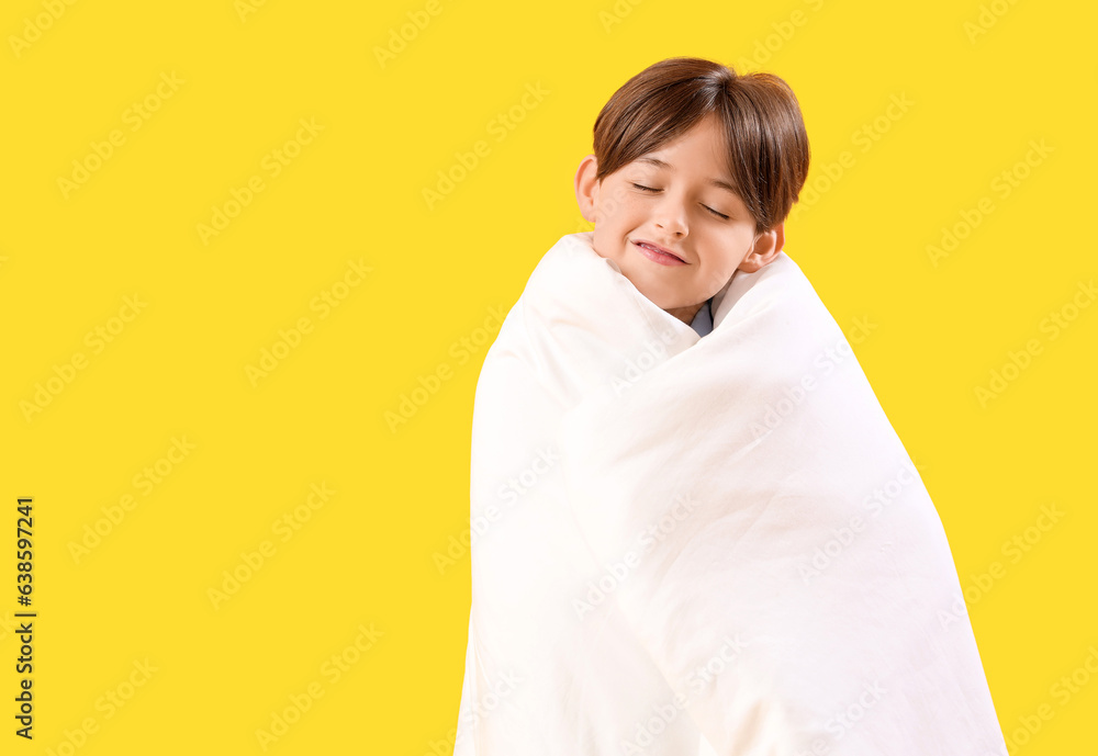 Little boy wrapped in blanket on yellow background