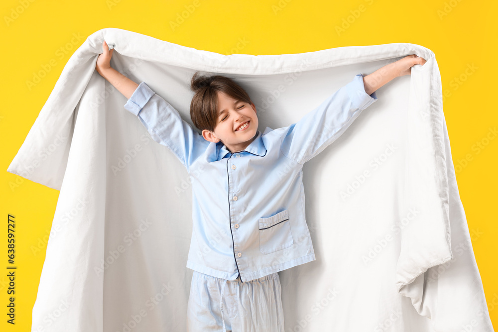 Cute little boy with blanket on yellow background