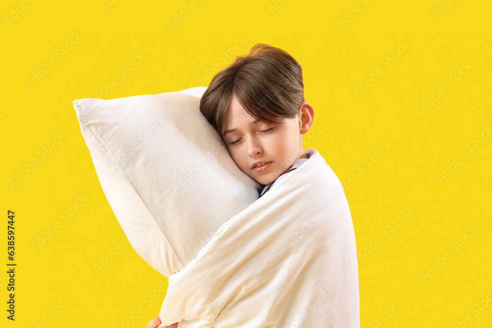 Sleepy little boy with pillow and blanket on yellow background