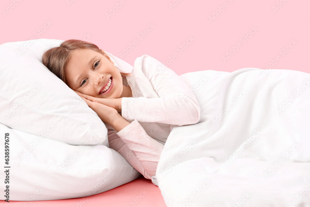 Little girl with pillow and blanket on pink background