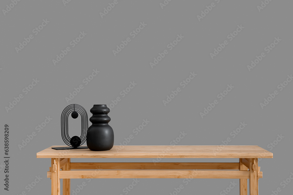 Wooden table with empty vase and decorative figure near grey wall