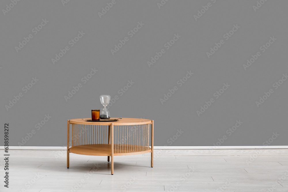 Tray with hourglass and candle on wooden coffee table near grey wall