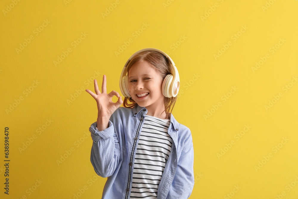 Little girl in headphones showing OK on yellow background