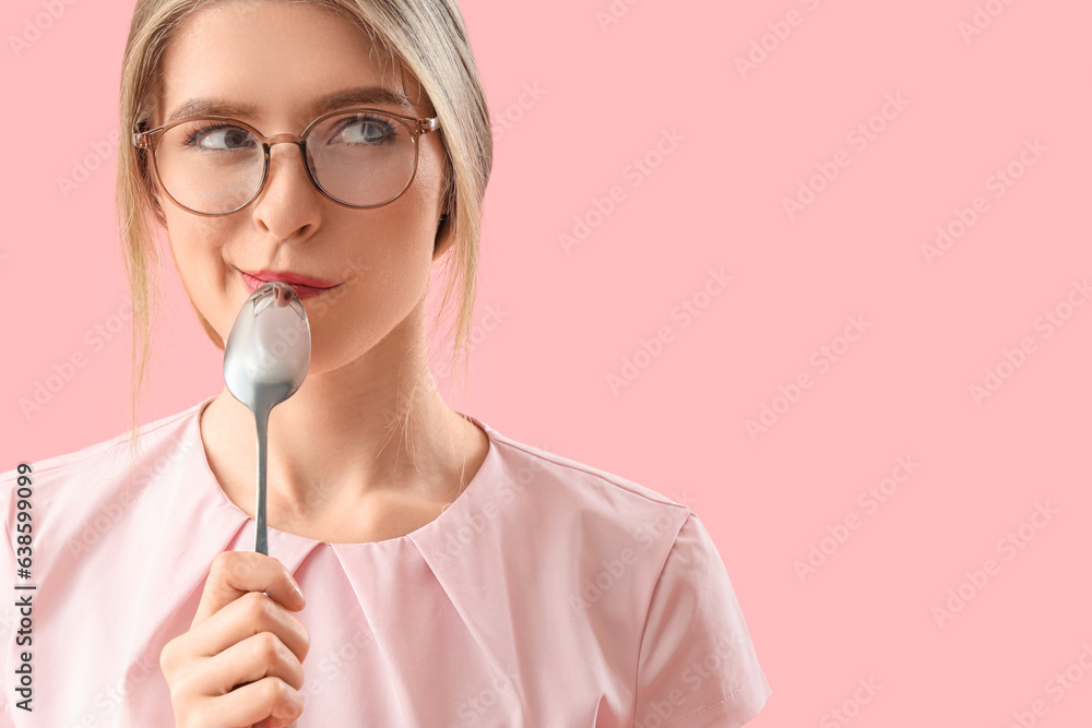 Thoughtful young woman with spoon on pink background, closeup