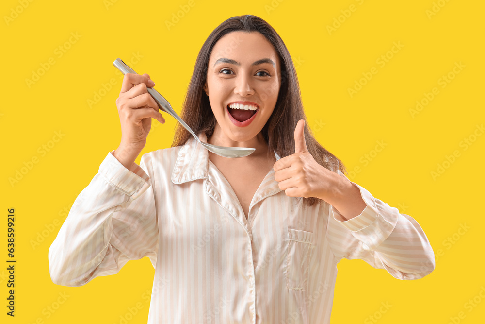 Young woman with ladle showing thumb-up on yellow background