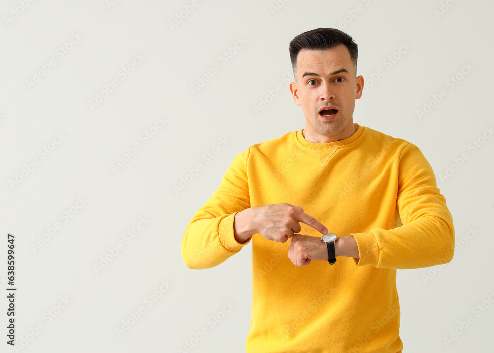 Stressed young man with wristwatch on light background. Deadline concept