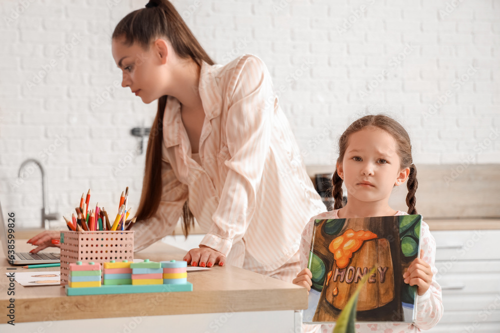 Sad little girl with book and her working mother in kitchen