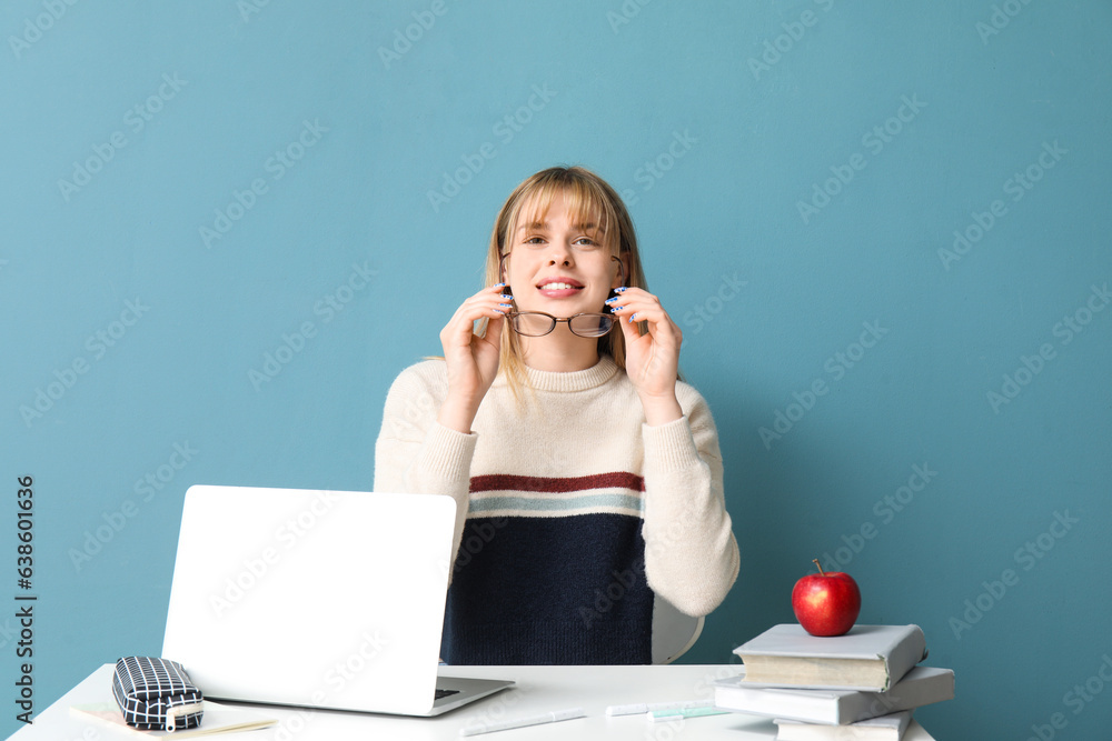 Female student doing homework at table on blue background