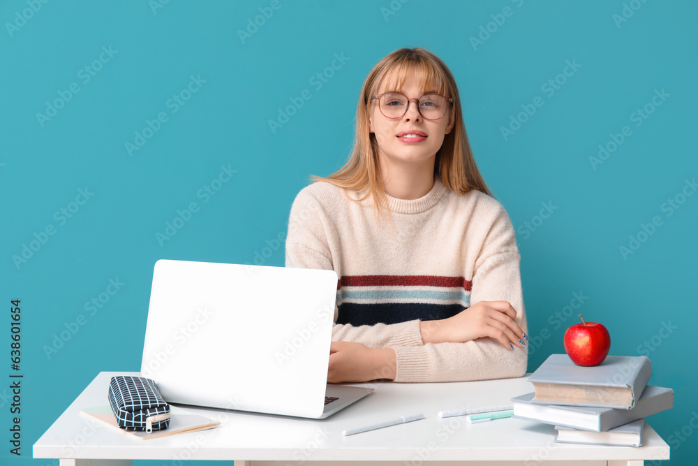 Female student doing homework at table on blue background