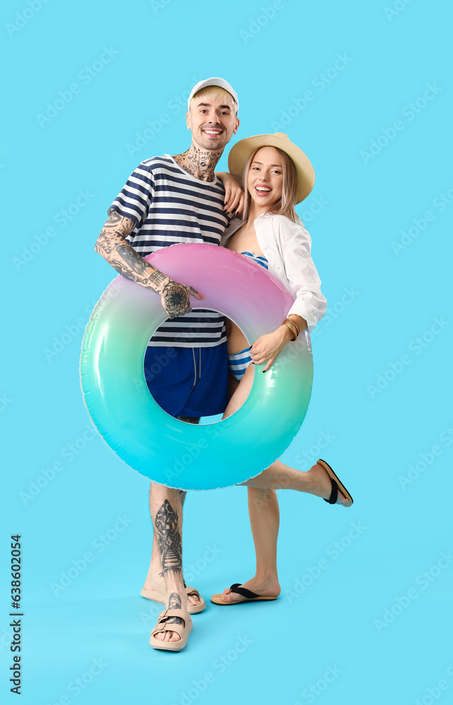 Young couple with inflatable ring on blue background