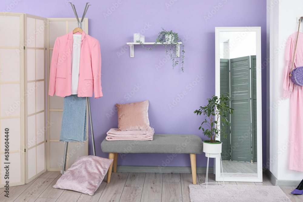 Interior of stylish hallway with mirror, rack and grey bench