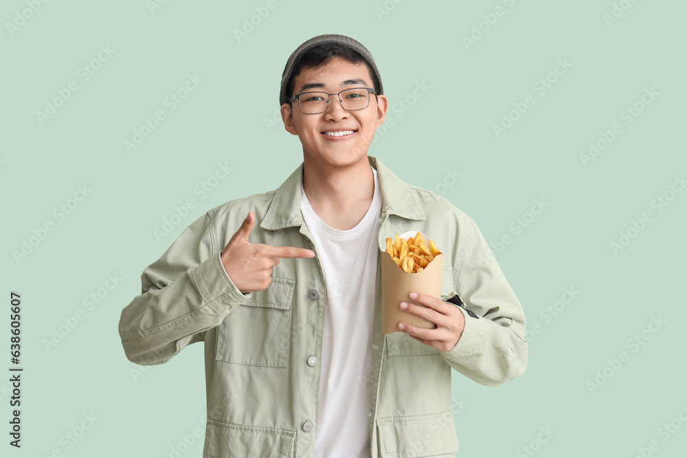 Young Asian man pointing at french fries on green background