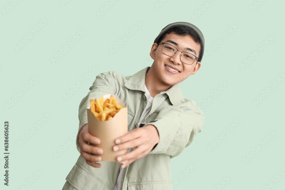 Young Asian man with french fries on green background