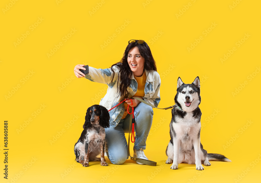 Young woman with cute dogs taking selfie on yellow background