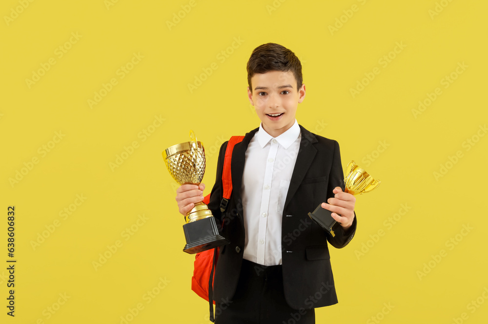 Smart little school boy with prize cups on yellow background