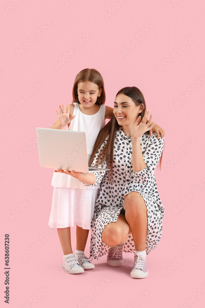 Happy mother with her little daughter using laptop on pink background