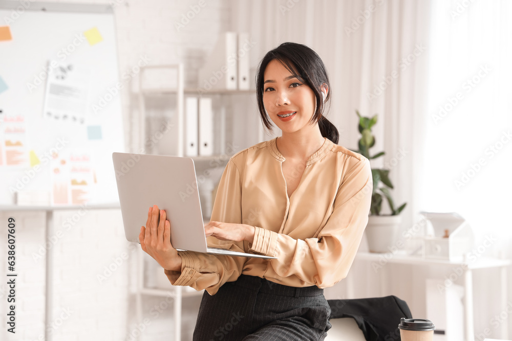 Happy Asian businesswoman working with laptop in office