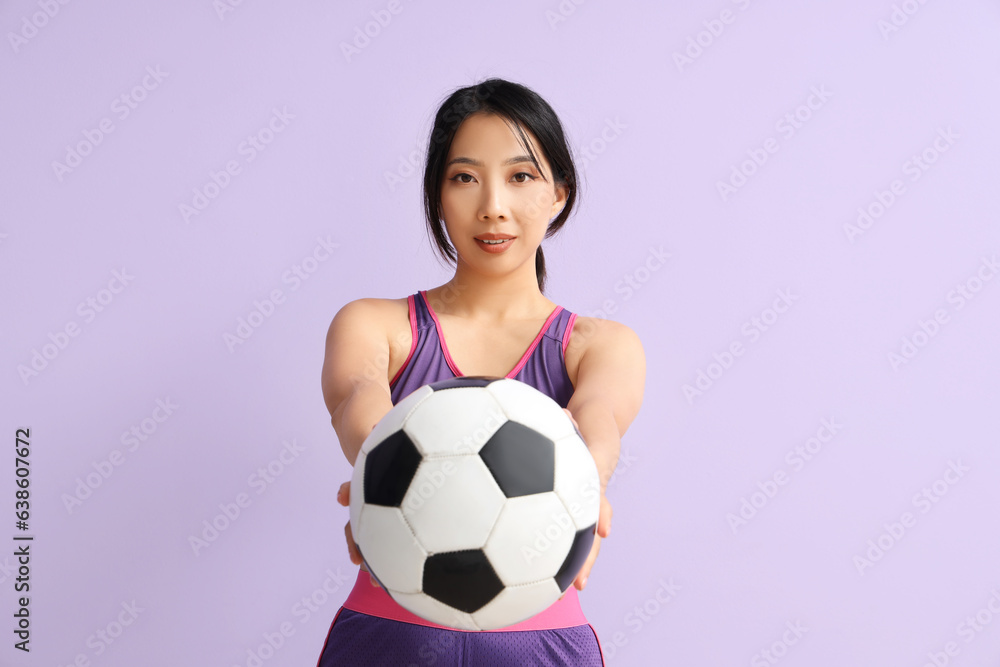 Happy young sporty Asian woman with soccer ball on purple background